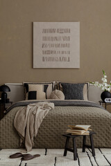 Modern bedroom with beige quilted bedding, patterned cushions, small stool with books and...