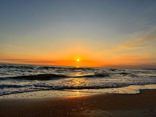 sunset at the beach, glowing sun, bright orange and blue sky with light waves
