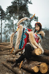 Obraz premium Woman in traditional costume aiming bow amidst logs in nature.