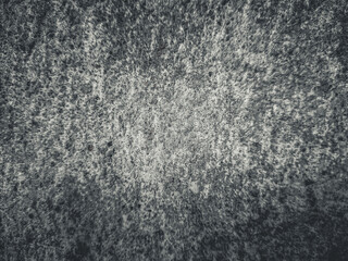 Gritty monochrome abstract background featuring a rough granular texture with a soft central focus...