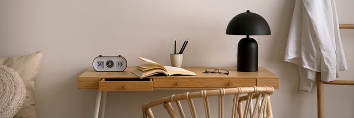 Minimalist composition of cozy bedroom with copy space, wooden desk, boho armchair, beige pillows, black lamp, clock, book and personal accessories. Home decor. Template.