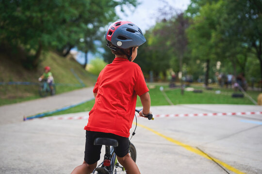 Young boy in red shirt riding bicycle with helmet in park, enjoying freedom and outdoor adventure on a sunny day