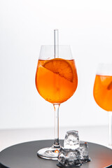 Glas mit leuchtend orangefarbenem Aperol Spritz Cocktail, verziert mit Eiswürfeln, einer frischen Orangenscheibe und einem stilvollen Trinkhalm