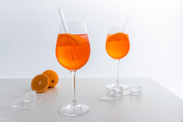 Glas mit leuchtend orangefarbenem Aperol Spritz Cocktail, verziert mit Eiswürfeln, einer frischen Orangenscheibe und einem stilvollen Trinkhalm