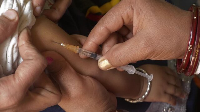 Social healthcare ASHA worker giving polio vaccine injection on arms of infant child to prevent poliovirus infections in rural Indian town, Begusarai, Bihar