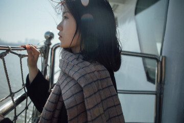 Woman in a checkered scarf gazing thoughtfully by the waterfront.