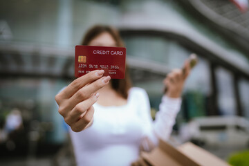 A happy young Asian woman smiles while holding shopping bags and a credit card, representing fashion, lifestyle, wealth, retail, and cheerful consumerism.