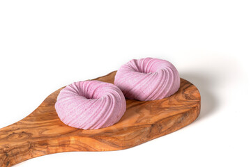 Two mousse pink pasties on a wooden texture board on a white table. Behind lies a sprig of...