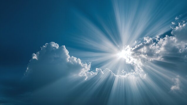 Bright sun rays piercing through fluffy white clouds in a clear blue sky with dramatic sunlight beams and radiant light shining from behind the clouds on a sunny day