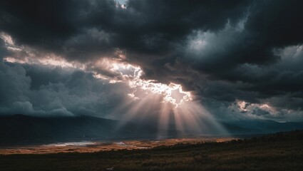 Dark clouds breaking apart with sun rays streaming down over a vast mountainous landscape during an atmospheric and dramatic sunset scene in the wilderness