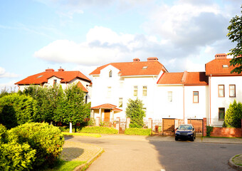 House in suburban neighborhood. Two story suburb house with garage. Blossom landscape at family house. Fence of home at street with pavement road. Car parked on empty street in residential area.