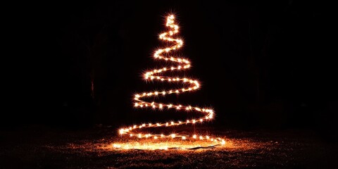 A spiral of warm, orange Christmas lights forms a tree shape on a dark surface. The lights are arranged in a tight, winding pattern, creating a glowing, abstract tree. 