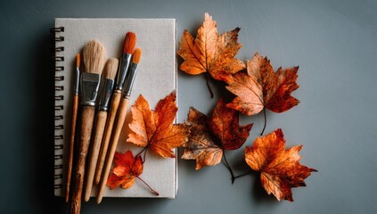 Autumnal art supplies.  Paint brushes and dried leaves rest on a notebook