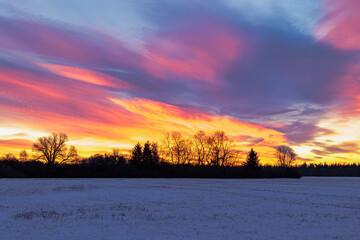 Colourful sunrise with glowing red clouds on a winter's day over the meadows and forests of Siebenbrunn, the smallest district of the Fugger city of Augsburg