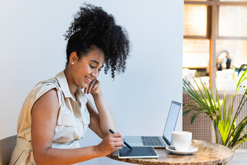 Smiling woman with curly hair working on graphic tablet in cafe