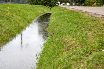 Water drainage ditch along rural roadside after rain with green grass and shallow water