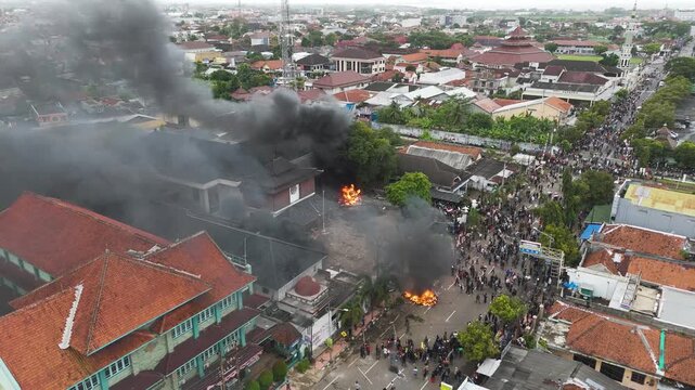 Cilacap, Indonesia- August 30, 2025: Burning dpr building burning building with crowds and smoke overwhelms the city street scene.
