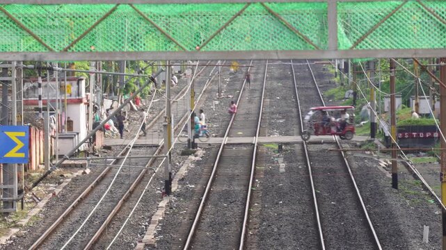 A set of parallel railway tracks, several vehicles and people are crossing through the railway crossing
