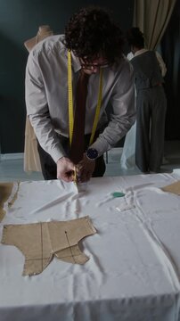 Young male fashion designer cutting white fabric, then pinning it to mannequin, creating gown in atelier