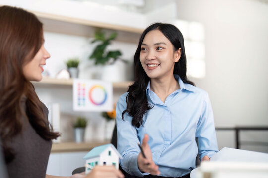 Engaging Conversation. Female architects discussing innovative home design with model.