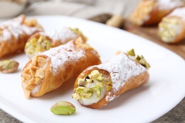 Delicious cannoli with ricotta cheese, peanuts, pistachios and powdered sugar on grey textured table, closeup