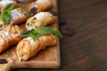 Delicious cannoli with cheese, nuts, chocolate, mint and powdered sugar on wooden table, closeup. Space for text