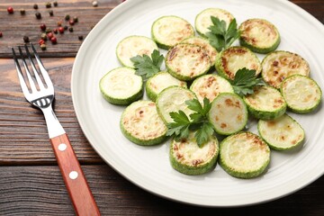 Delicious fried courgette slices with parsley served on wooden table, closeup