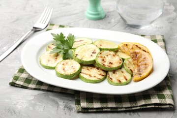 Delicious fried courgette slices with lemon and parsley served on grey table, closeup