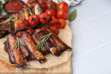 Roasted beef ribs with rosemary, tomatoes and sauce on white tiled table, closeup