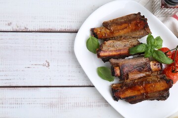 Roasted beef ribs, tomatoes and basil on white wooden table, top view. Space for text