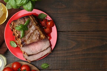 Delicious baked beef meat, tomatoes and basil on wooden table, flat lay. Space for text