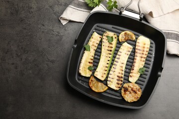 Delicious grilled courgette slices with garlic, lemon and parsley in pan on grey textured table,...