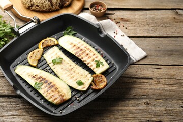 Delicious grilled courgette slices with spices and lemon in pan on wooden table, closeup