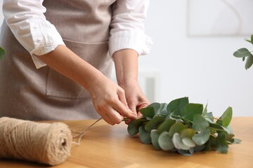 Florist making beautiful bouquet of eucalyptus branches at wooden table in flower shop, closeup