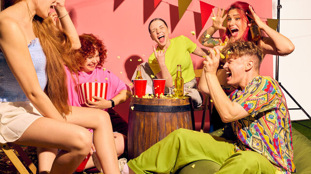 Young friends laughing while throwing popcorn at each other at party in cheerful playful moment. Concept of pop culture, gen z celebration, food and beverage fun, friendship, and entertainment joy.