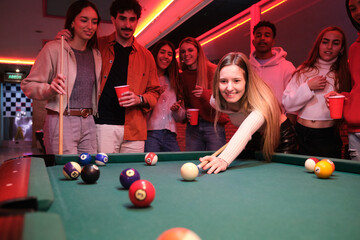 Young people enjoying a game of pool in a bar, drinking and having fun