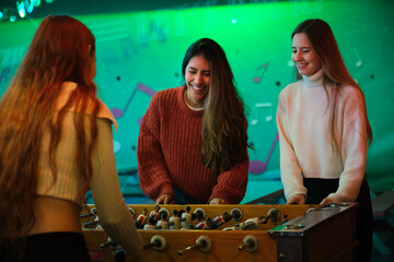 Three young women enjoying a friendly game of foosball, having fun and laughing together in a...