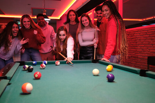 Group of young friends playing pool in a club, having fun together