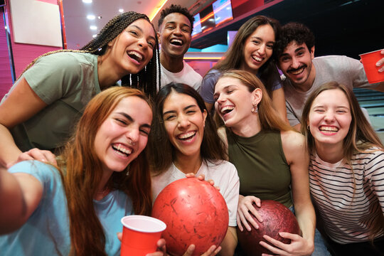 Group of cheerful young friends taking selfie and having fun at bowling alley