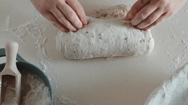 Close-up video of hands folding, rolling, and sealing bread dough into an oval batard on a floured kitchen counter for proofing.