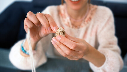A woman holds a beautiful stone with a hole in her hand and threads a rope through it to create an original necklace. She smiles and enjoys
