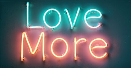 Neon sign displays words Love More. Turquoise, orange hues illuminate dark background. Positive message, simple design.