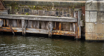 The side of a canal near a wooden inlet gate with the depth measurements carved in roman numerals....