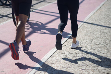 Fototapeta premium Two people and their shadows are seen running along a beach during strong sunlight. Healthy sports practice.
