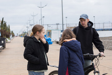 Pretty child girls 10 and 12 years old and her father with bicycle walking outdoors
