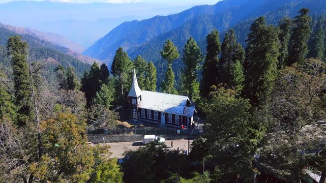 Aerial view of St. Matthew's Church nestled between lush green trees and mountains, a serene landscape with a white van parked nearby, Nathia Gali, Pakistan.