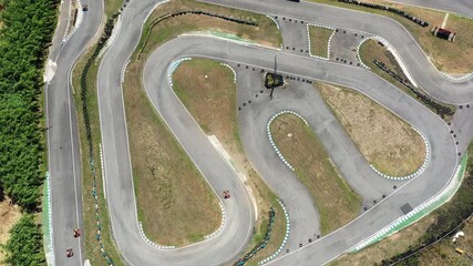 Aerial top down drone view of go kart racing on winding track with karts navigating sharp turns at high speed. open wheel kart motorsport competition on asphalt circuit