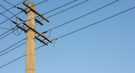 青空の下、無数の電線が伸びる木製の電柱が力強くそびえ立つ。