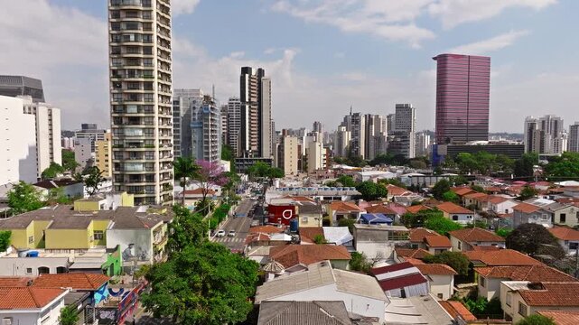 Drone flying forward over Vila Madalena, S&atilde;o Paulo, on a sunny day, rising to reveal houses, buildings, trees, cars, and the city skyline in the background