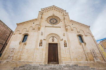 Daytime panoramic view of the historic town of Matera in southern Italy. The image highlights ancient stone houses, narrow streets, and the iconic Matera Cathedral rising above the Sassi cave dwelling